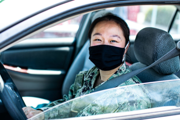 A woman sitting in the front seat of a car wearing a black face mask and a military uniform