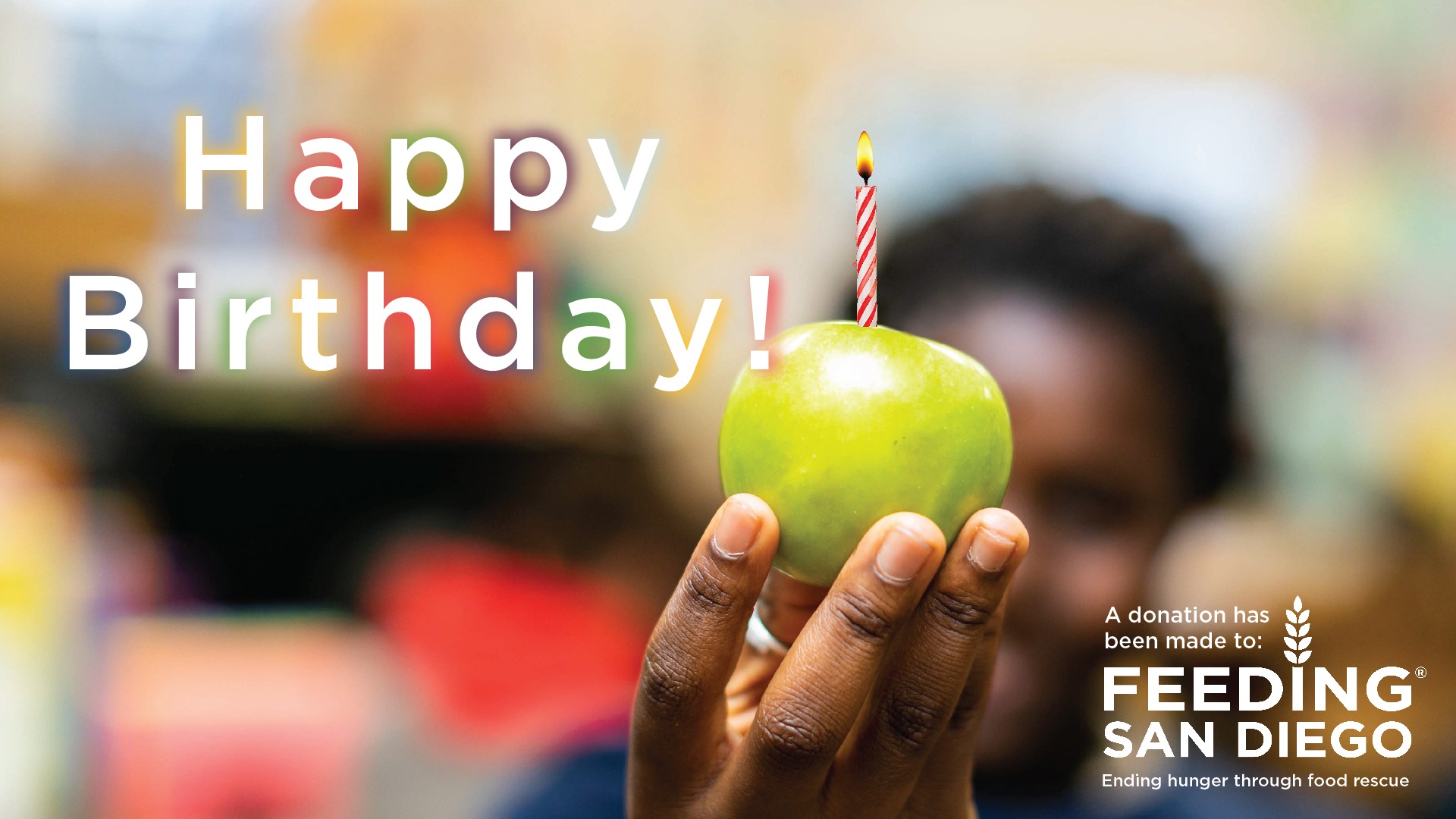 An e-card with a photo of a hand holding an apple with a birthday candle in it and text that reads Happy Birthday! A donation has been made to Feeding San Diego