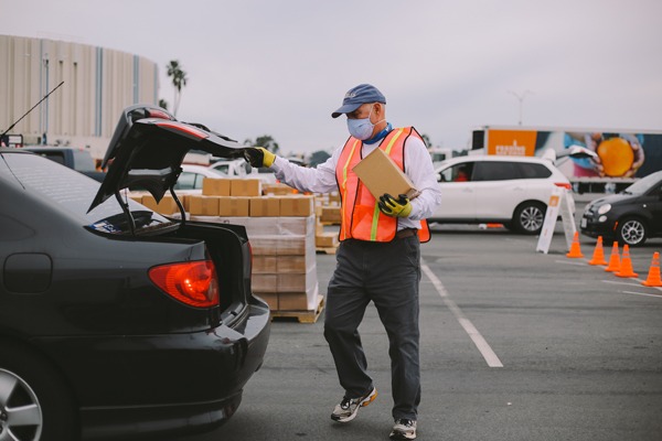 Volunteer loads box of food into trunk of car at large scale distribution