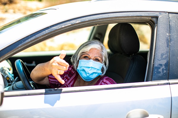 Older woman in car showing Shaka