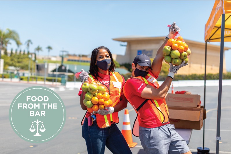 Volunteers holding bags of fruit at distribution with logo of Feeding San Diego campaign Food from the Bar