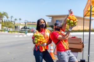 Volunteers hold bags of apples and oranges at Feeding San Diego distribution