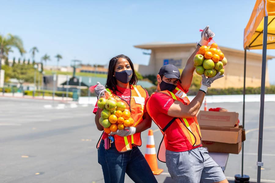 Volunteers hold bags of apples and oranges at Feeding San Diego distribution