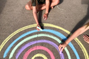 Hands drawing a chalk rainbow on the sidewalk