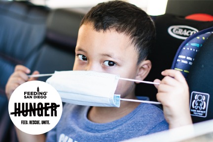 Boy pulls mask over his face while waiting in car at Feeding San Diego food distribution with logo for Feeding San Diego campaign Cross Out Hunger