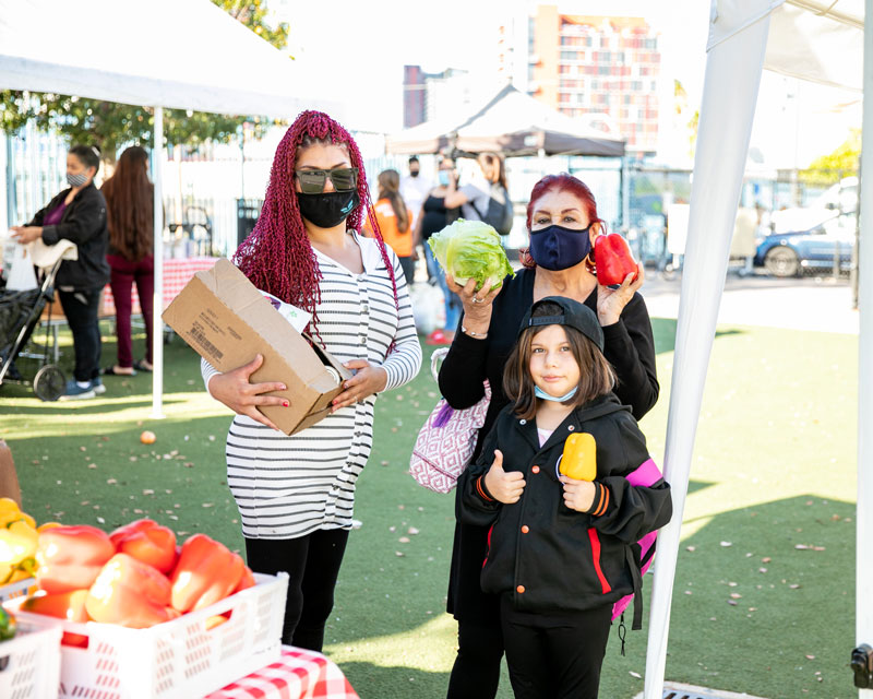 Two women and a young child hold produce at a Feeding San Diego food distribution