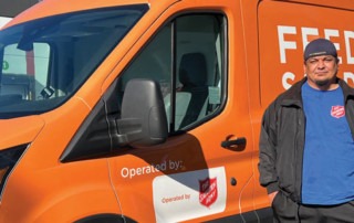 Daniel, a formerly homeless man, stands in front of an orange Feeding San Diego food rescue van