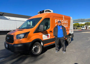 Daniel, a formerly homeless man, stands in front of an orange Feeding San Diego food rescue van