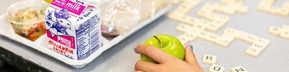 A school lunch tray and a hand holding a green apple