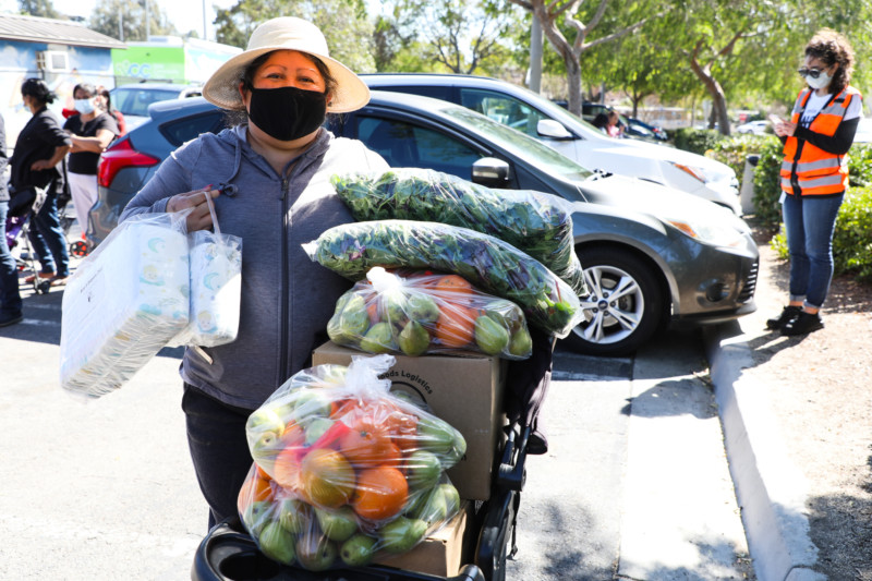 A woman stands next to a cart filled with fresh produce at a food distribution from one of Feeding San Diego's community partners