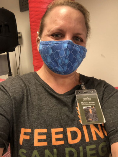 A woman wearing a blue mask and a gray shirt with a Feeding San Diego reoccurring volunteer badge