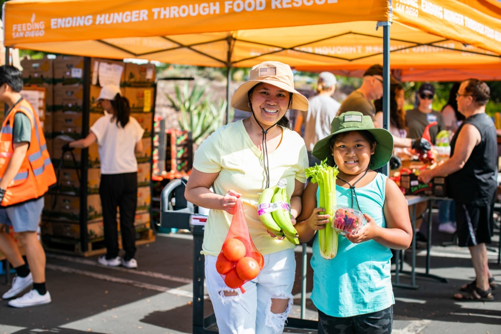 A woman and a young girl hold produce at a Feeding San Diego food distribution