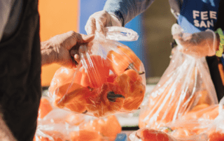 A volunteer in a Feeding San Diego apron hands a bag of orange peppers to a man at a Feeding San Diego mobile pantry