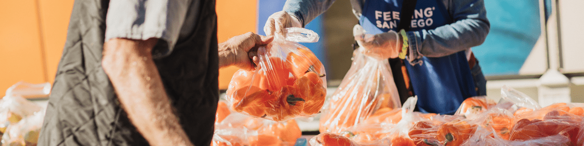 A volunteer in a Feeding San Diego apron hands a bag of orange peppers to a man at a Feeding San Diego mobile pantry