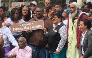 A group of people in a park holding a sign that says "Honorary Theresa Mae Saunders"