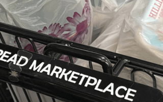 A shopping cart with a bag of food and the words "Daily Bread Marketplace" on the handle