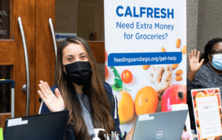 Three women waving next to a sign that says "CalFresh - Need Extra Money for Groceries?"