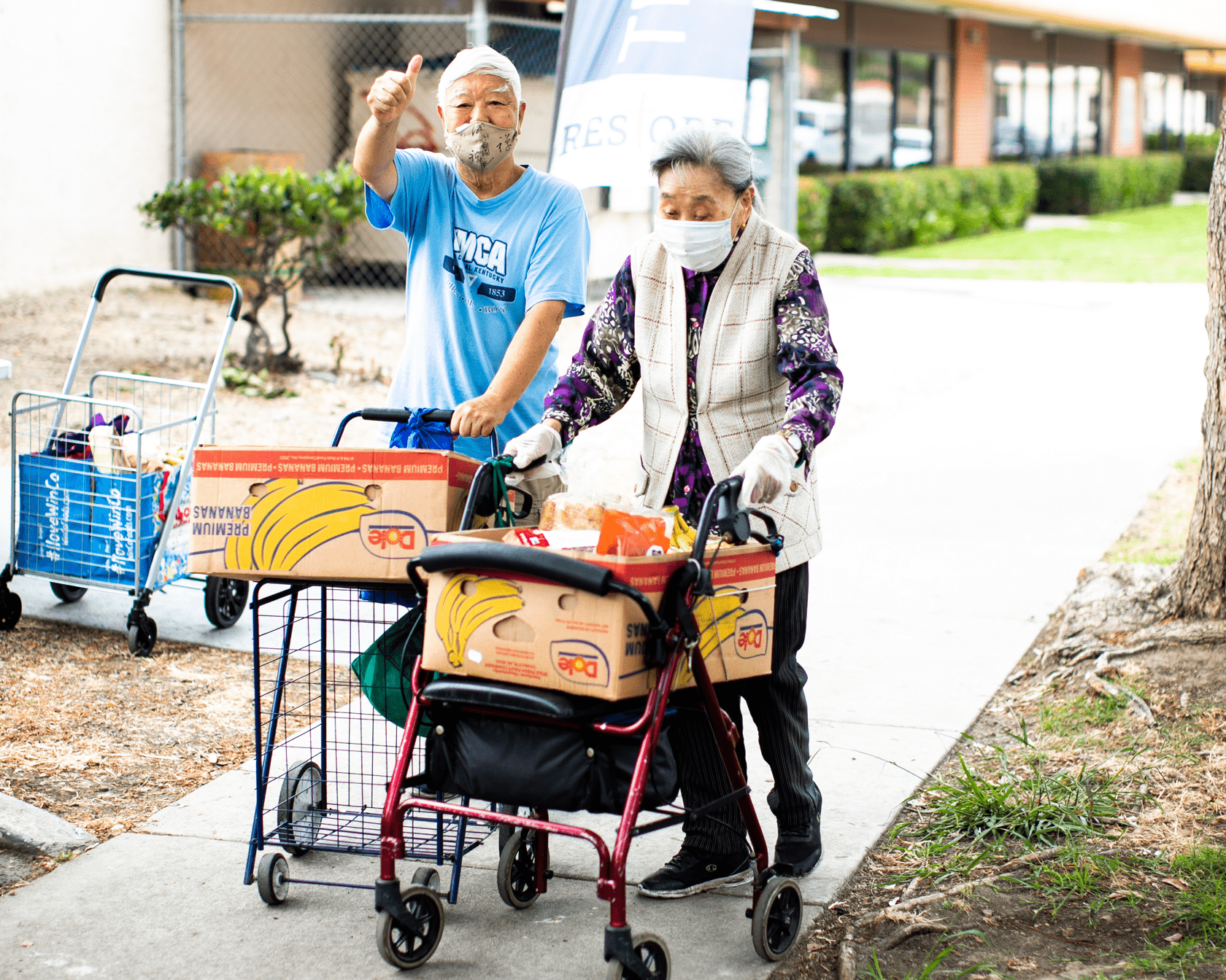 A senior couple pushing carts with boxes of food from a Feeding San Diego food distribution