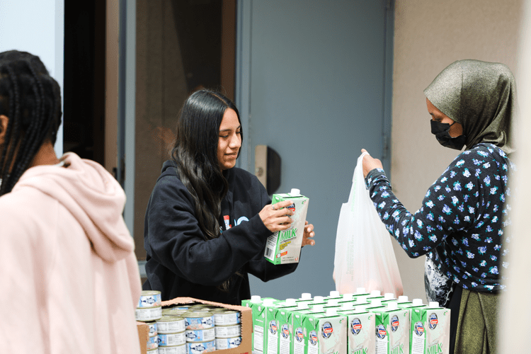 A girl hands a box of milk to a woman with a head scarf at a school pantry