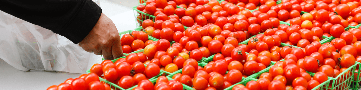 A hand places a basket of cherry tomatoes next to other baskets