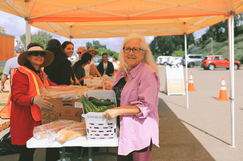 A woman with long white hair holding a box of produce