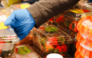 A gloved hand sets a container of strawberries with other food