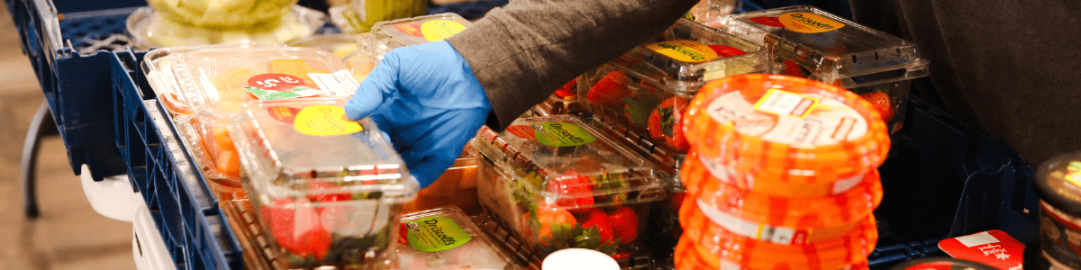 A gloved hand sets a container of strawberries with other food