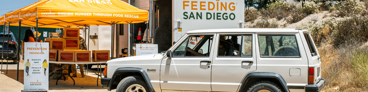 A car parked in front of a Feeding San Diego pop-up and truck