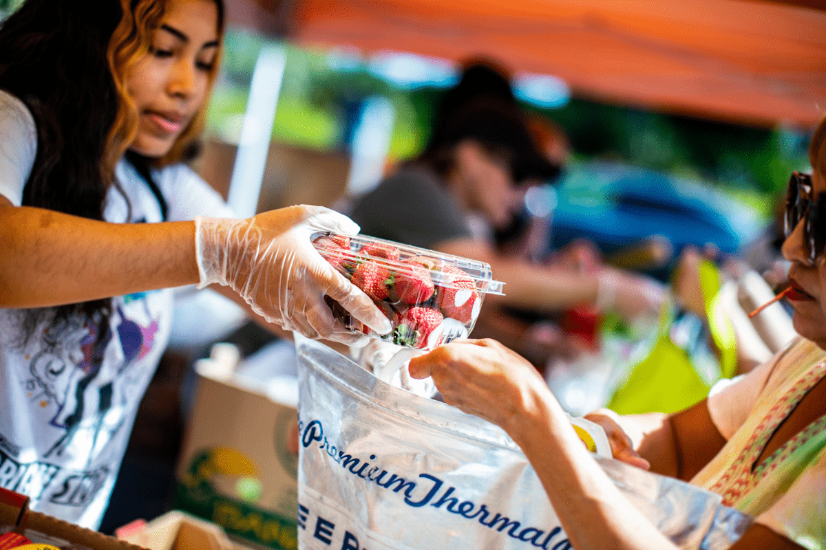 A volunteer hands a package of strawberries to a food distribution attendee