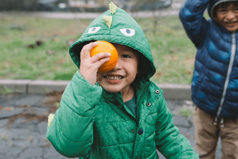 A boy in a dinosaur hoodie holding an orange