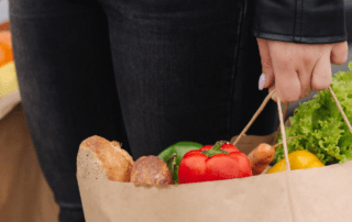 Hands carrying grocery bags filled with fresh produce