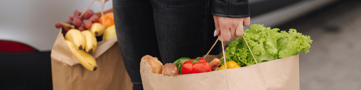 Hands carrying grocery bags filled with fresh produce