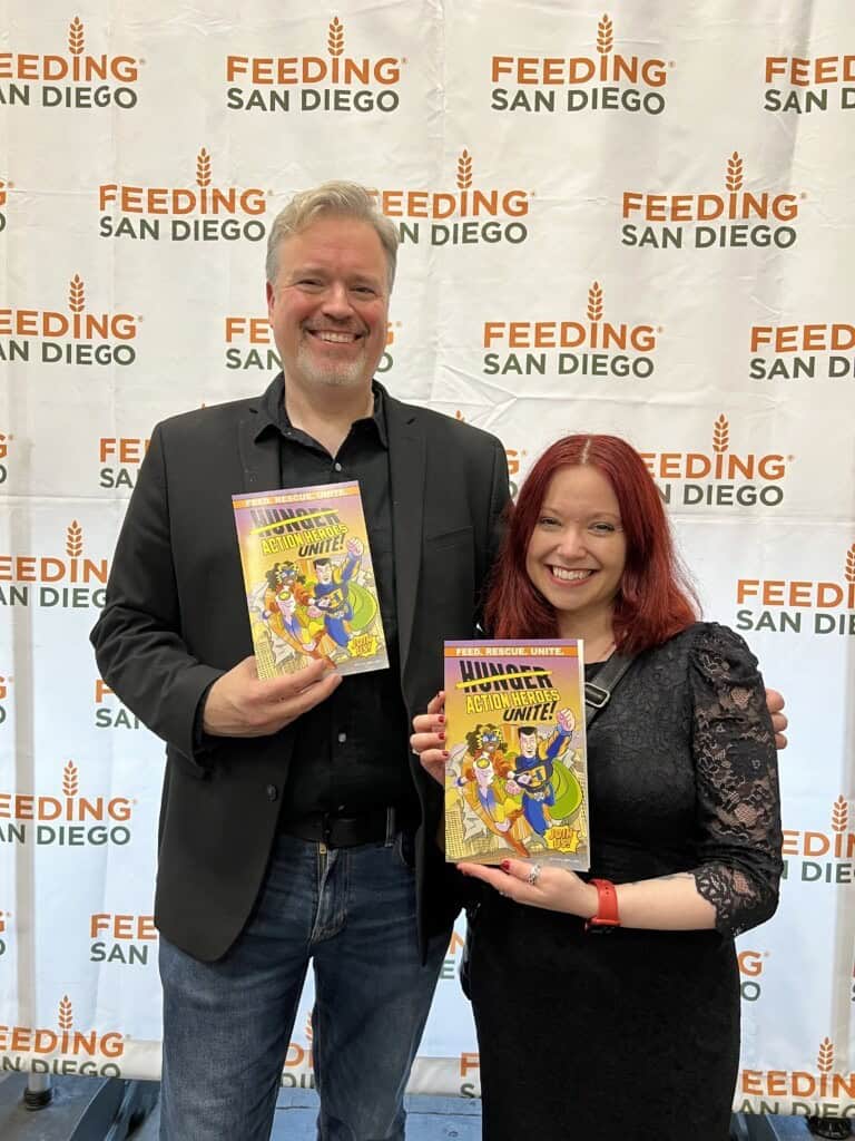 Man and woman smiling while holding the Hunger Action Heroes Unite Comic Book