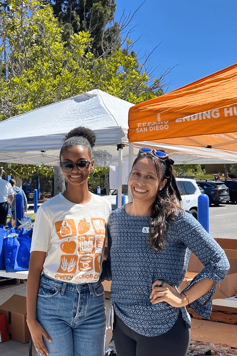 Two smiling women stand in front of pop-up tents at a Feeding San Diego school pantry