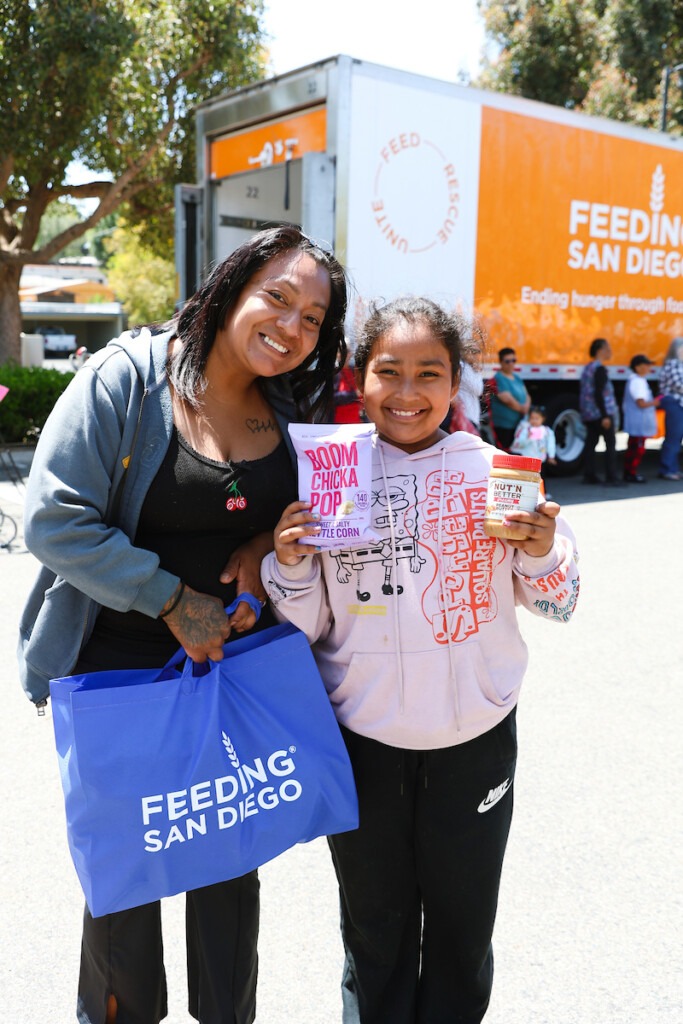Agency enews – portrait – family A woman and a young girl holding food and smiling with at Feeding San Diego truck in the background