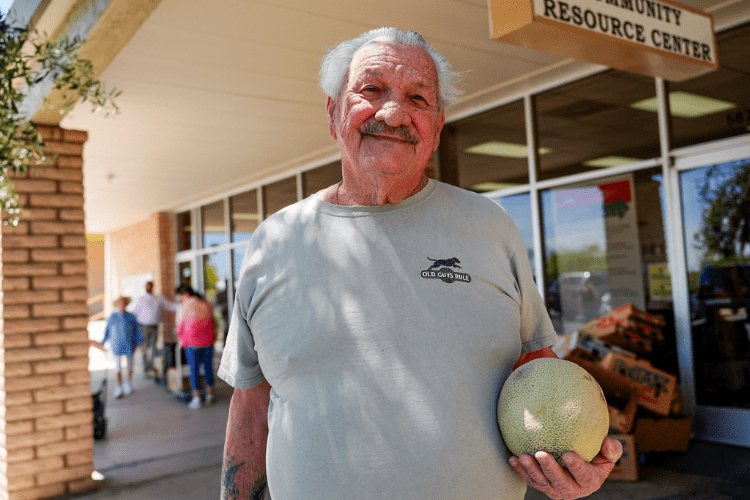 A smiling man with white hair holding a melon