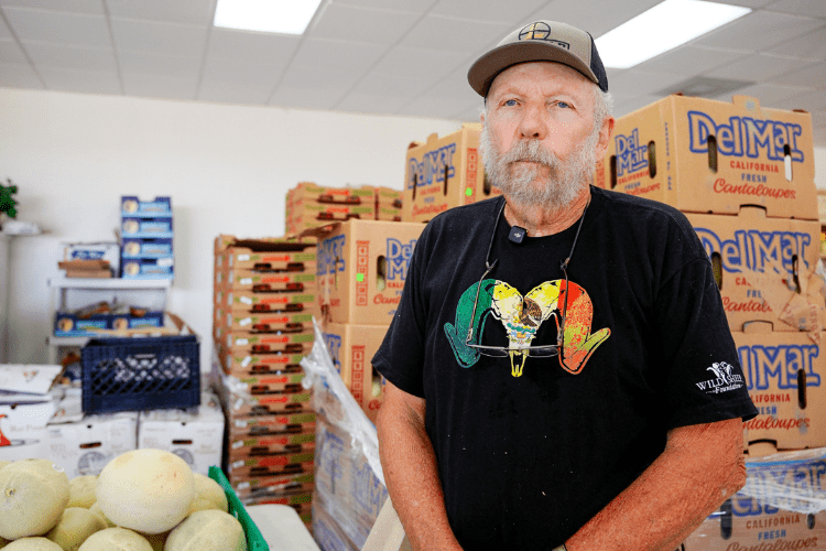 A man with a white beard sitting in a room with boxes of produce