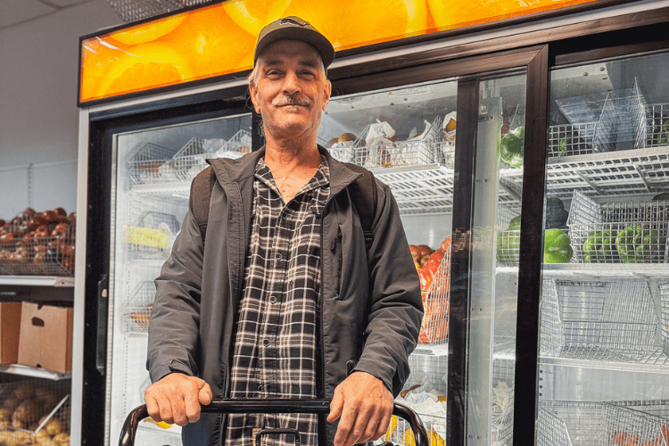 A man with white hair stands with a cart of food in the Feeding San Diego Marketplace
