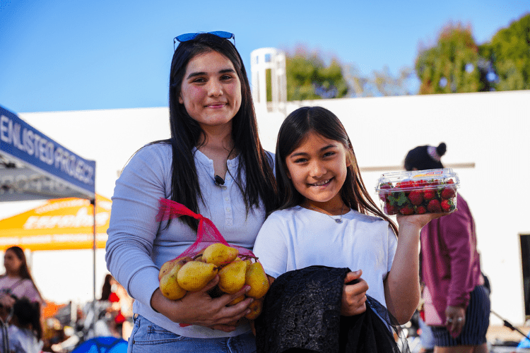 A smiling woman and a young girl holding fresh produce